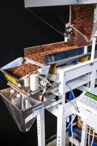 Close-up of coffee beans in an industrial roasting machine with a control panel.