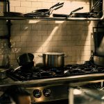 pexels-photo-17303438 A well-equipped restaurant kitchen with pans and pots on a stove under warm lighting.